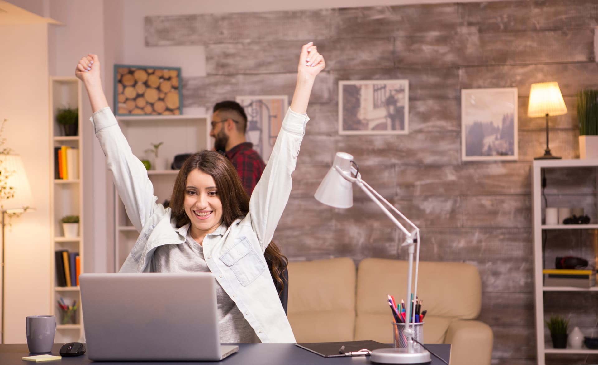 A freelancer celebrates with her hands raised after reading the good news on her laptop